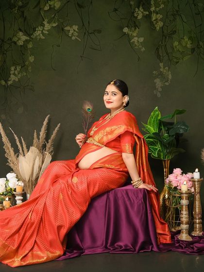 Another beautiful solo shot from a traditional maternity session. The mom-to-be, dressed in a red silk saree, holds a peacock feather, adding a touch of divine symbolism to the portrait.