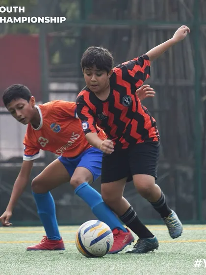 This action shot captures the essence of youth football: two determined players giving their all to win the ball for their team.