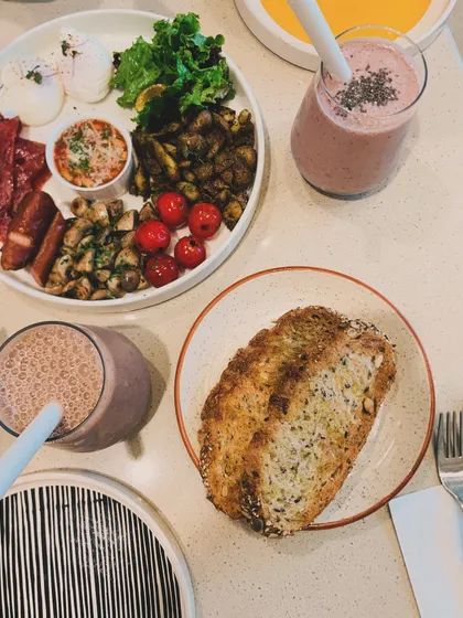 A top-down view of a hearty brunch spread. It features our full breakfast plate with eggs, sausages, and mushrooms, alongside toasted sourdough and smoothies.