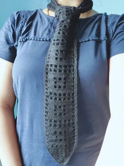 This is a filet crochet tie, a unique and modern accessory for a formal or semi-formal look. The openwork pattern adds a touch of handmade elegance.