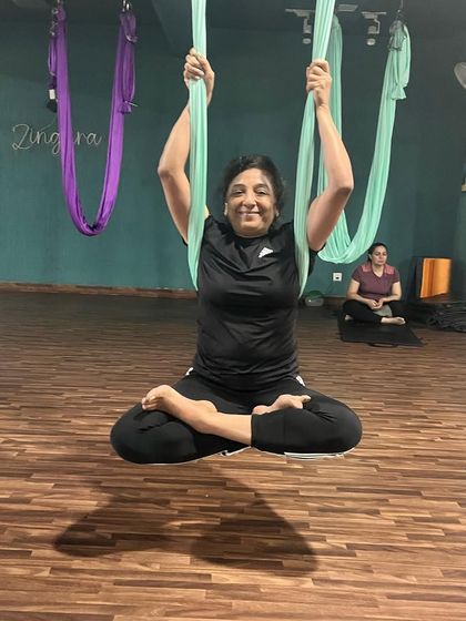 A smiling member enjoying the floating lotus pose. This image perfectly captures the sense of accomplishment and peace that our aerial yoga classes bring to the Zingara Tribe.