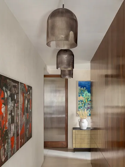 This passageway in the House of Terraces features rich wood-paneled walls and dramatic pendant lighting. We use corridors as opportunities to create atmosphere and showcase art, making every part of the home feel considered.