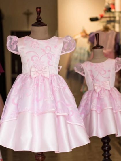 These matching pink gowns are perfect for a special occasion. The design features layers of organza with a delicate print and a sweet bow, created in two sizes for sisters.