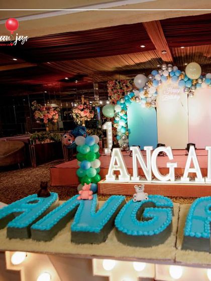 A grand first birthday for Angad! This setup features a large stage with a pastel balloon arch, marquee letters, and a custom cake spelling out the birthday boy's name.