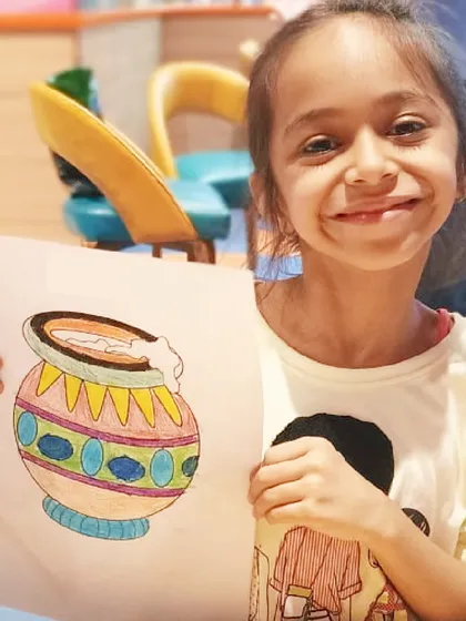 A girl proudly displays her colorful drawing of a matki. Our Janmashtami workshops include themed art projects that connect kids with the stories and symbols of the festival.