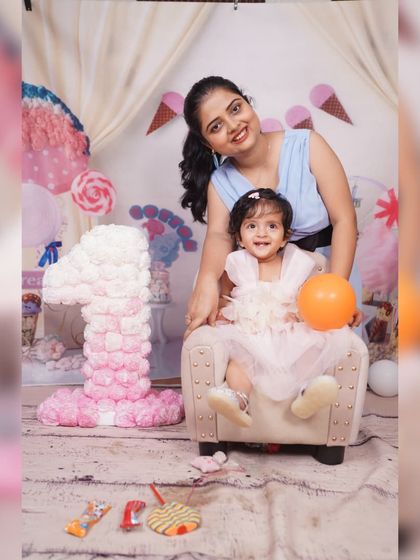 A mother and daughter portrait in the Candy Land themed set. The decor includes a large floral '1' prop and various candy-themed elements to create a sweet scene.