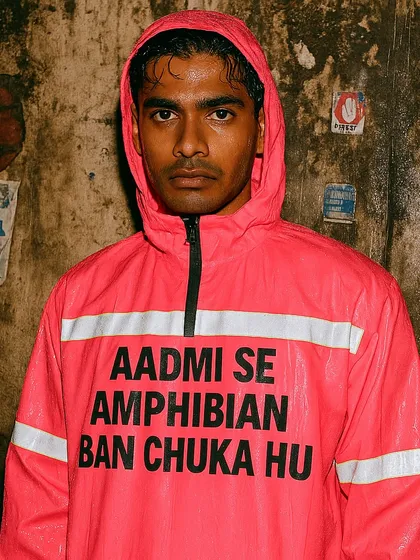 A man in a pink raincoat that says 'AADMI SE AMPHIBIAN BAN CHUKA HU'. This 'Rainquotes' piece humorously describes the feeling of evolving to survive the annual city floods.