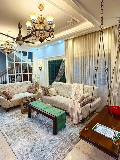 A living room that perfectly fuses Indian heritage with European classicism, featuring a traditional wooden jhula (swing) and elegant wall mouldings.