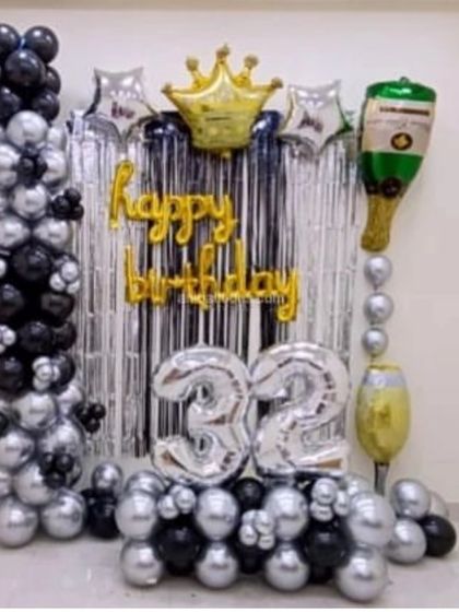 A fun black and silver theme for a 32nd birthday. This compact setup includes a shimmer curtain, balloon columns, and foil balloons for the age, a crown, and a champagne bottle.