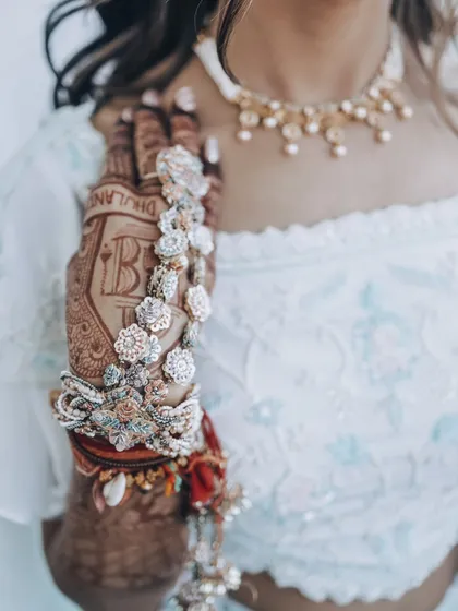 A detailed close-up of the bride's hands, showcasing the intricate floral jewelry and mehendi design.