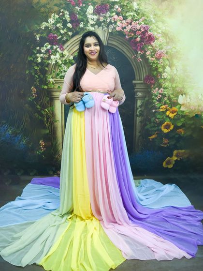 A happy mom-to-be in our rainbow gown, holding up a pair of blue and pink baby shoes to celebrate her twins.