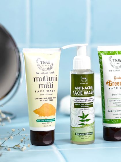 A close-up of three face wash products against a blue bathroom tile backdrop. The styling with a mirror and delicate flowers adds a touch of freshness and suggests a refreshing cleansing experience.