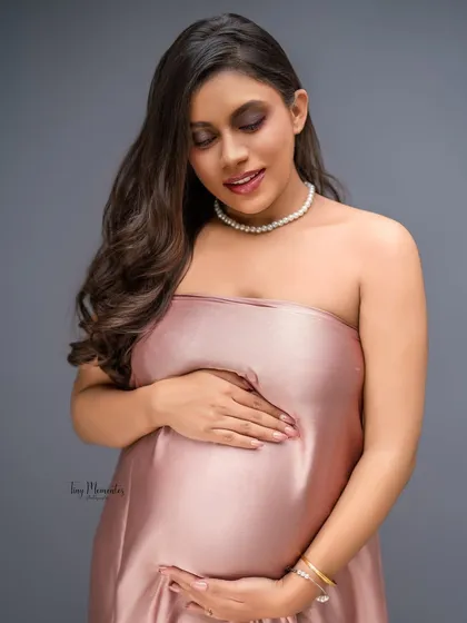 A close-up portrait that captures the soft texture of the satin gown and the mother's gentle, loving gaze towards her baby bump.