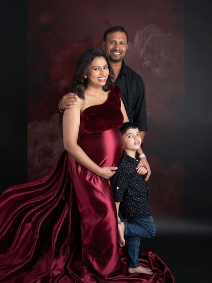 A beautiful family portrait in rich, warm tones. The mom-to-be's wine-red gown coordinates perfectly with the dark, moody backdrop, creating a very elegant look.
