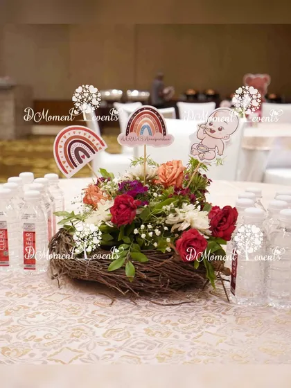 A unique table centerpiece for the Annaprashan ceremony. A bird's nest holds a small floral arrangement with themed cutouts, surrounded by personalized water bottles for guests.