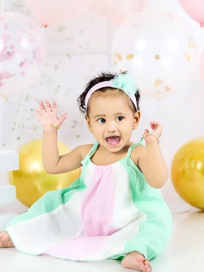 A baby girl throws her hands up in excitement during her first birthday photoshoot. Her joyful expression is priceless.