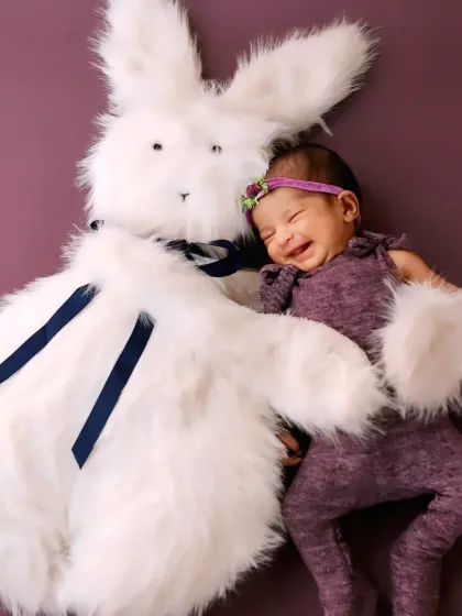 A heartwarming shot of a smiling newborn snuggling with a large, fluffy white bunny toy.