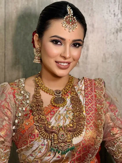 A beautiful portrait of a bride with a radiant smile. The makeup is classic South Indian, with heavy temple jewelry and a warm, glowing complexion.