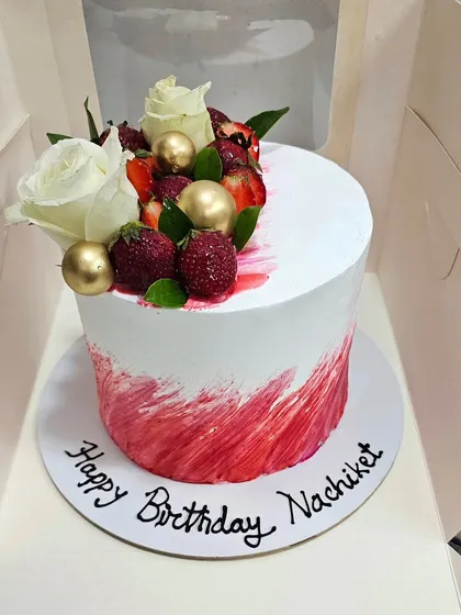 A "Strawberry Blast" cake with a red and white textured buttercream finish, topped with fresh strawberries, roses, and gold spheres.