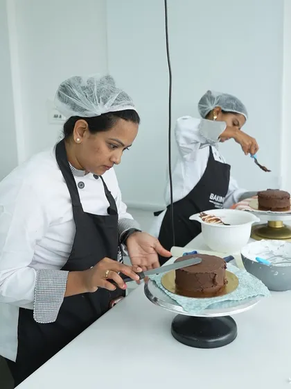 In our classes, every student works at their own station. This image shows a student concentrating on getting a smooth, even layer of chocolate frosting, a fundamental skill for professional cake decorating.