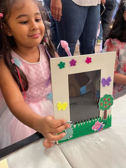 A proud little girl holding up the Peppa Pig-themed photo frame she decorated herself. It's a wonderful keepsake from a fun-filled birthday party.