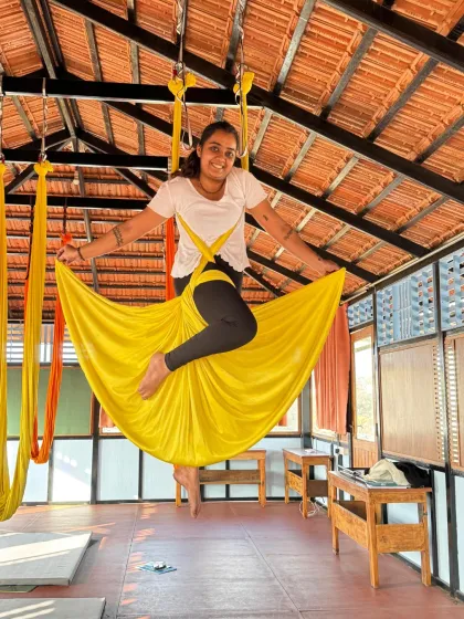 A student joyfully sits in the hammock in a skirt pose, embodying the playful and liberating spirit of aerial yoga.