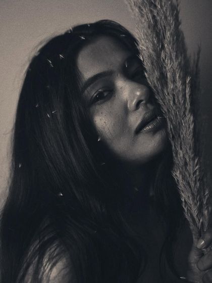 This portrait has a soft, melancholic feel. The model's downward gaze and the way she holds the pampas grass create a sense of introspection. The grainy black and white finish adds to the poetic mood.