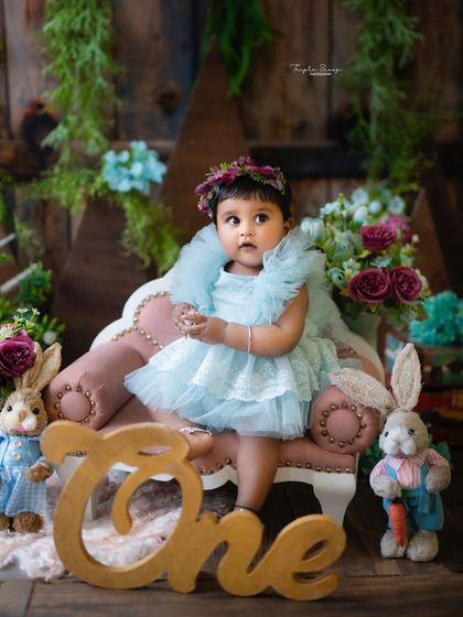 A rustic woodland-themed first birthday portrait. The wooden 'One' sign and adorable bunny props create a charming and whimsical atmosphere.