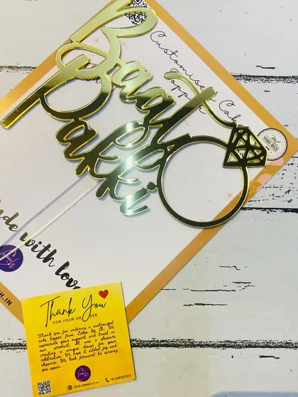 A close-up of the "Baat Pakki" topper, showing the detail of the ring and the script.