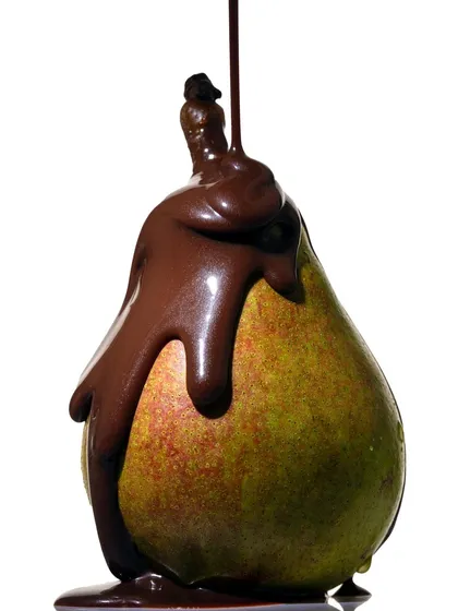 A slightly different take on the chocolate-covered pear, capturing the drip and flow of the liquid. The hard lighting creates strong highlights on the chocolate, emphasizing its rich, smooth surface.