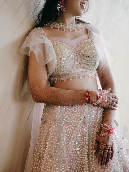 A close-up shot focusing on the bride's gorgeous Sangeet outfit. The mirror work on the blouse and her intricate mehndi are beautifully detailed.