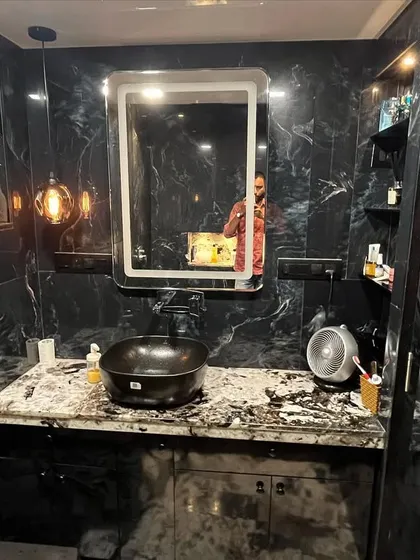 A luxurious bathroom design featuring black marble-patterned tiles on all walls. The space includes a custom vanity with a vessel sink, a backlit mirror, and accent pendant lighting for a dramatic effect.