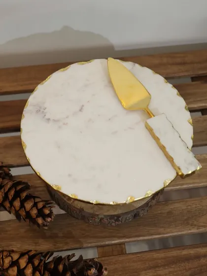 Our white marble cake platter with a gold-leafed edge and matching server, resting on a rustic wood slice. This piece combines natural textures with luxe details for a stunning effect.