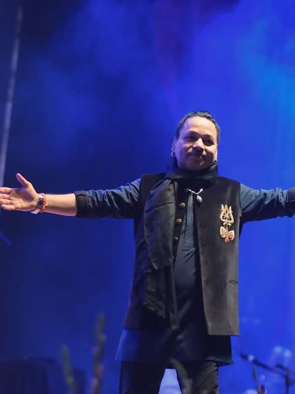 An open-armed welcome from Kailash Kher to the audience. The blue smoke and stage lights create a mystical atmosphere that perfectly complements his music.