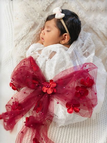 A close-up of a sleeping baby wrapped with a beautiful red bow for her first Christmas photoshoot. The details make these holiday milestone pictures so special.