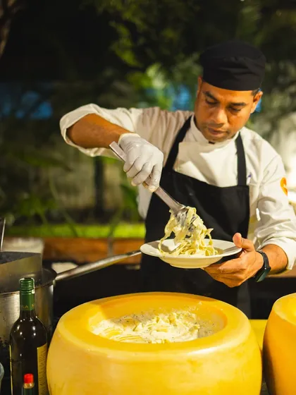 A chef serves a plate of creamy pasta directly from the Parmesan cheese wheel.