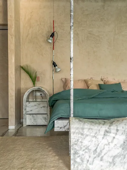 A floating bed and bedside table, both crafted from Grey Myst marble, create a sense of lightness in this bedroom. The raw, textured walls provide a warm, earthy contrast to the cool, polished marble.