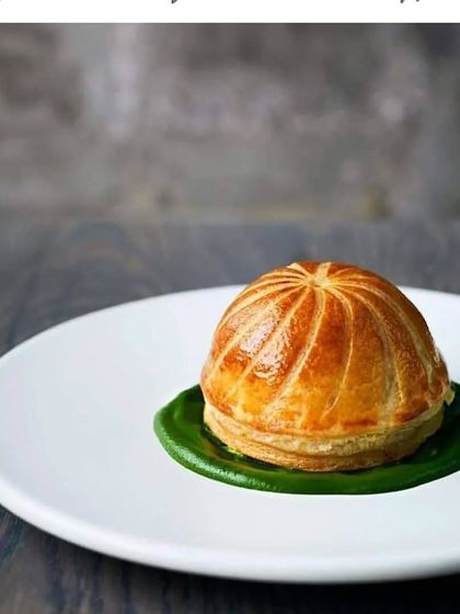 We excel at creating gourmet appetizers that showcase culinary technique. This dish features a perfectly baked puff pastry dome on a bed of vibrant green sauce, offering a fine-dining experience in a single bite.