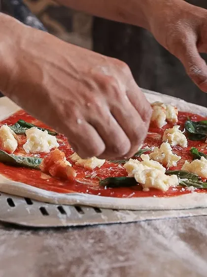 Our chef carefully places hand-torn pieces of our fresh mozzarella onto a Margherita pizza. This step is crucial for achieving the perfect melt and distribution of cheese.