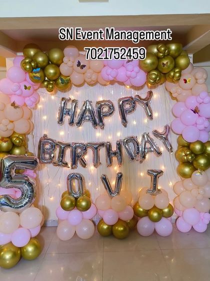A lovely home setup for a 5th birthday. The pink and gold balloon arch frames a backdrop with fairy lights and "Happy Birthday" foil letters.