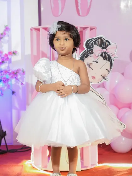 A custom-designed white party dress perfect for a milestone birthday celebration. This piece features a modern one-shoulder design with a sequined bodice and a full, fluffy tulle skirt, ensuring the birthday girl feels like the star of her special day.