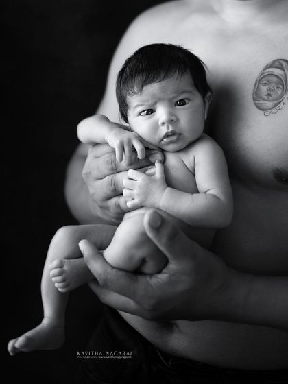 A nine-day-old baby girl looks up at her father, her tiny body resting safely in his hands. A powerful black and white portrait of their first connection.