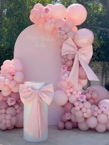 An elegant outdoor setup with a focus on texture, featuring large fabric bows on the backdrop and plinth, all in a soft pink palette.