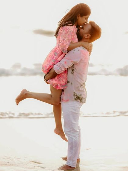 A playful and romantic moment on the beach, with the groom lifting the bride for a kiss against the setting sun.