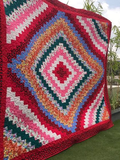 A stunning "log cabin" quilt with a diamond-in-a-diamond pattern, displayed outdoors.