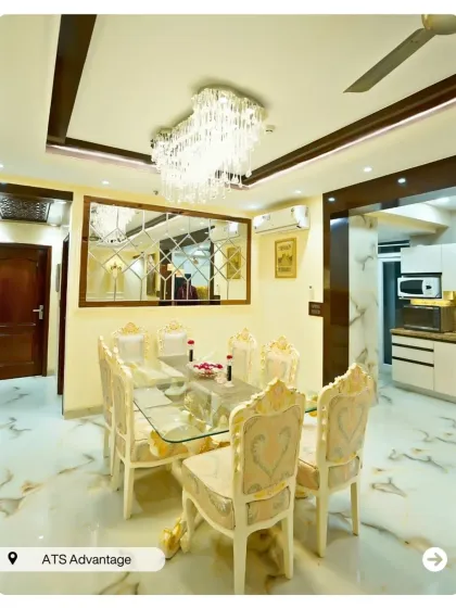 A luxurious dining room with a glass-top table and ornate, gold-accented chairs. The large mirrored wall panel makes the space feel larger and more opulent.