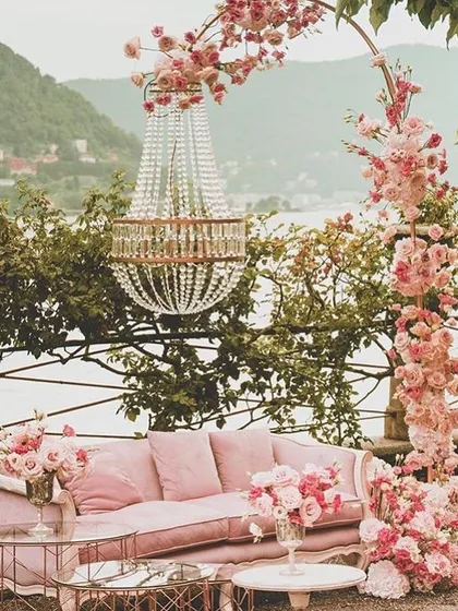 A romantic and picturesque seating area by the water, with a pink vintage sofa, a crystal chandelier, and beautiful floral arrangements.