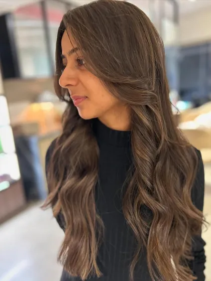 A side view of this beautiful first-time hair color. The long face-framing layers and balayage highlights create a soft and flattering look.