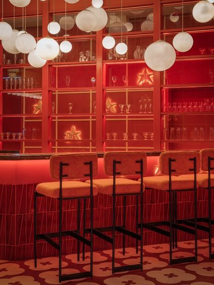 The bar area at Masala is a feast for the eyes. The combination of glowing red shelves, orange upholstered bar stools, and a cluster of pendant lights creates a focal point that is warm, inviting, and full of energy.