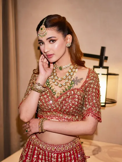 This shot highlights the beautiful contrast of green jewelry against the rich red lehenga, a classic combination that always feels fresh and sophisticated.